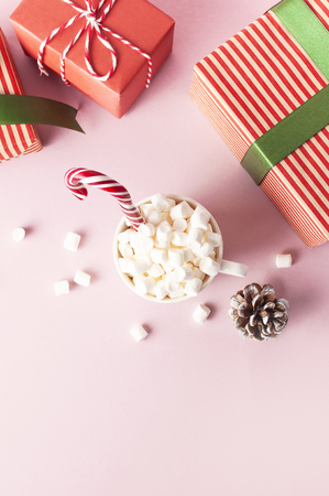 White mug with marshmallows Candy Cane gifts boxes with green ribbon on pink background Flat Lay Winter traditional drink food Festive decor Christmas New Year presents Xmas holiday.の写真素材