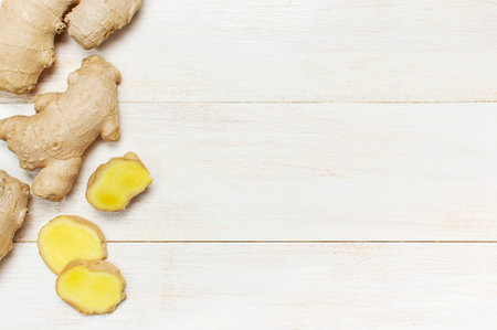 Whole and sliced fresh ginger roots on white wooden background top view copy space. Minimalistic...