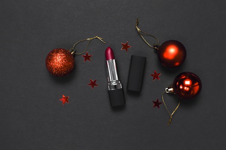 Red lipstick, Christmas balls, confetti on black background top view flat lay copy space. Professional Makeup and Beauty. Fashionable bright lipstick closeup. Make-up new year christmas conceptの写真素材