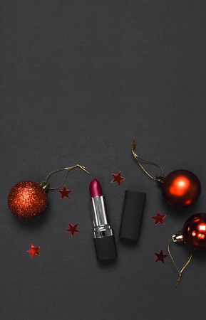 Red lipstick, Christmas balls, confetti on black background top view flat lay copy space. Professional Makeup and Beauty. Fashionable bright lipstick closeup. Make-up new year christmas conceptの写真素材