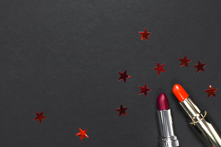 Red lipstick, holographic confetti on black background top view flat lay with copy space. Professional Makeup and Beauty. Fashionable bright lipstick closeup. Beautiful Make-up conceptの写真素材