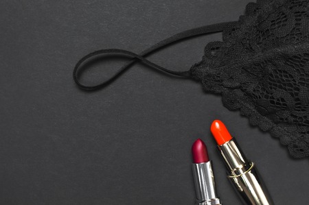 Black lace bra underwear, red lipstick on dark background top view flat lay. Female essential erotic accessories, fashionable underwear gift for birthday valentines day new year christmasの写真素材