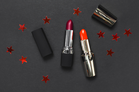 Red lipstick, holographic confetti on black background top view flat lay with copy space. Professional Makeup and Beauty. Fashionable bright lipstick closeup. Beautiful Make-up conceptの写真素材
