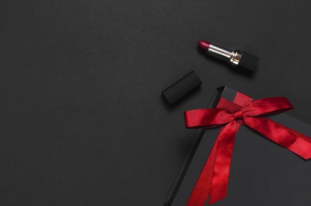 Black gift box with red ribbon, lipstick on dark background top view flat lay. Holiday concept, birthday gift, Valentine's Day, presents. Congratulations background. Beautiful dark Make-up conceptの写真素材