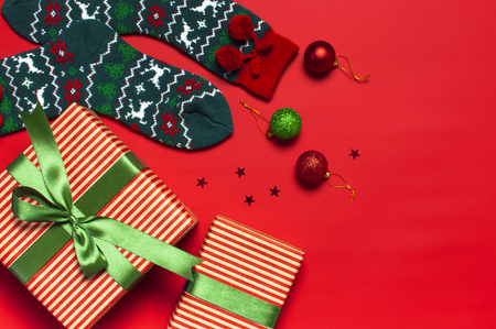 Woolen socks with a Christmas New Year ornament, gift box, balls, glitter confetti on red background top view flat lay. Holiday concept, presents Xmas. Congratulations background with space for textの写真素材