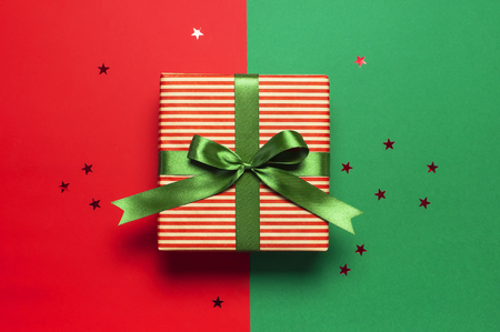 Gift boxes with green ribbon and holographic glitter confetti form of stars on red green background top view flat lay space for text. Holiday concept, new year or Christmas gift box, presents Xmasの写真素材