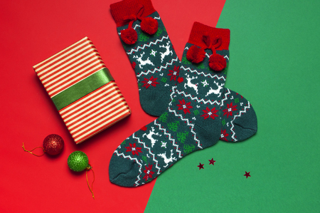 Woolen socks with a Christmas New Year ornament, gift box, balls, glitter confetti on red green background top view flat lay. Holiday concept, presents Xmas. Congratulations background space for textの写真素材