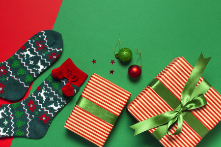 Woolen socks with a Christmas New Year ornament, gift box, balls, glitter confetti on red green background top view flat lay. Holiday concept, presents Xmas. Congratulations background space for textの写真素材