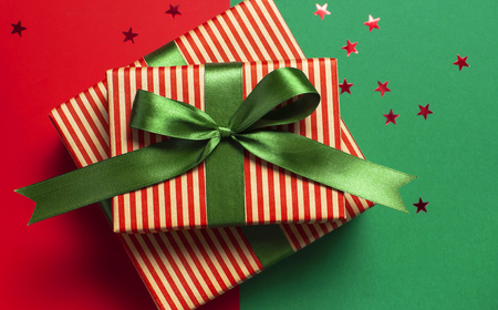 Gift boxes with green ribbon and holographic glitter confetti form of stars on red green background top view flat lay space for text. Holiday concept, new year or Christmas gift box, presents Xmasの写真素材