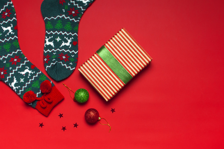 Woolen socks with a Christmas New Year ornament, gift box, balls, glitter confetti on red background top view flat lay. Holiday concept, presents Xmas. Congratulations background with space for textの写真素材