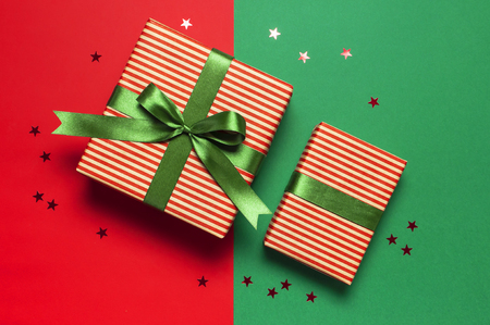 Gift boxes with green ribbon and holographic glitter confetti form of stars on red green background top view flat lay space for text. Holiday concept, new year or Christmas gift box, presents Xmasの写真素材