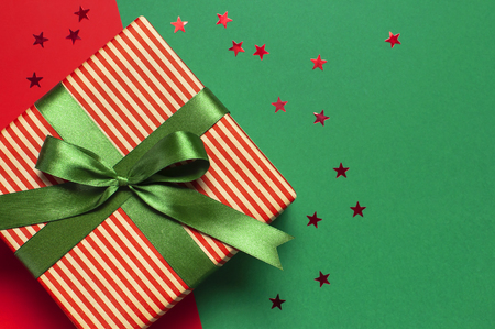 Gift boxes with green ribbon and holographic glitter confetti form of stars on red green background top view flat lay space for text. Holiday concept, new year or Christmas gift box, presents Xmasの写真素材