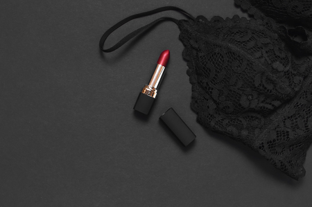 Black lace bra underwear, red lipstick on dark background top view flat lay with copy space. Female essential erotic accessories, fashionable underwear, gift for birthday valentines day, shoppingの写真素材
