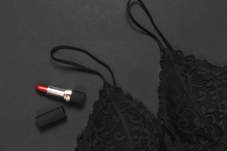 Black lace bra underwear, red lipstick on dark background top view flat lay with copy space. Female essential erotic accessories, fashionable underwear, gift for birthday valentines day, shoppingの写真素材