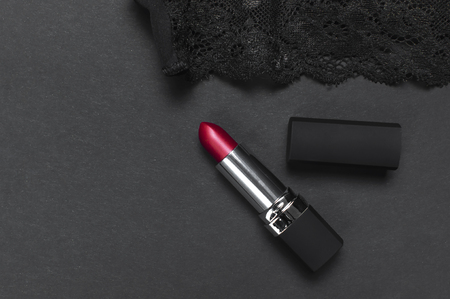 Black lace bra underwear, red lipstick on dark background top view flat lay with copy space. Female essential erotic accessories, fashionable underwear, gift for birthday valentines day, shoppingの写真素材