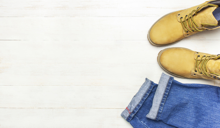 Men's casual wear, yellow work boots from natural nubuck leather, blue jeans and brown belt on wooden white background top view flat lay copy space. Trendy casual shoes, youth style, sale shopの写真素材