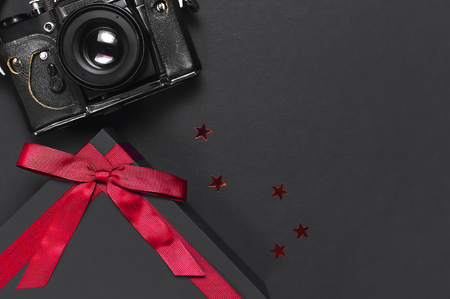 Old retro vintage camera, Black gift box with red ribbon on black background top view flat lay with copy space. Concept for the photographer, old photographic equipment minimalistic styleの写真素材