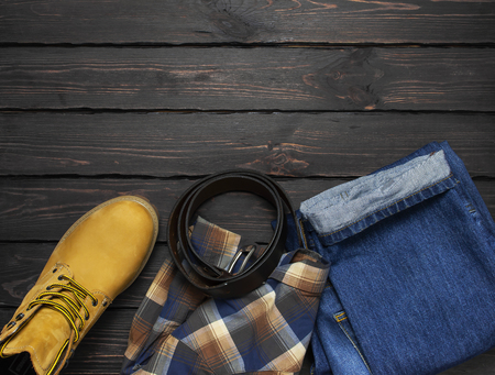 Men's casual wear, yellow work boots from natural nubuck leather, blue jeans, checkered shirt and brown belt on dark wooden background top view flat lay copy space. Trendy casual shoes, youth styleの写真素材