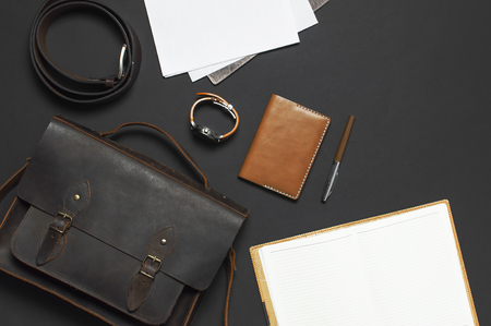 Fashionable concept. Brown leather men's bag, wristwatch, leather passport cover, pen, blank white sheets on black background top view flat lay with copy space Accessories businessman stylish clothesの写真素材