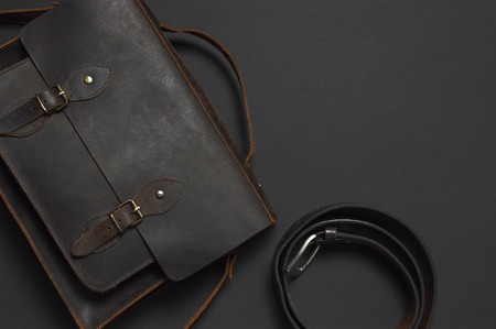 Fashionable concept. Brown leather men's bag, leather belt for trousers on black background top view flat lay with copy space. Briefcase for work, Accessories businessman stylish men's clothesの写真素材