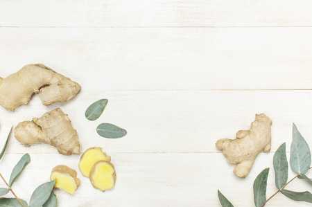 Whole and sliced fresh ginger roots, eucalyptus on white wooden background top view copy space. Minimalistic style, seasoning spice ingredient for tea Concept healthy food medicine improving immunityの写真素材
