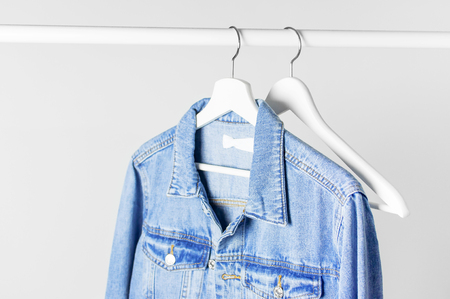 Blue denim jacket on white wooden coat hanger on a rod against light gray wall flat lay copy space. Denim, fashionable jacket, women's or men's trend clothing, fashion background. Store concept, saleの写真素材