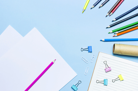 Wooden colored pencils, clean school notebook in line, paper clips on blue background top view flat lay copy space. Pencils for drawing, objects for creativity. Back to school conceptの写真素材