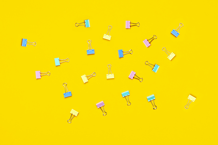 Multicolored paper clips on bright yellow background top view flat lay copy space. Minimalistic office background, education, objects for creativity. Back to school conceptの写真素材