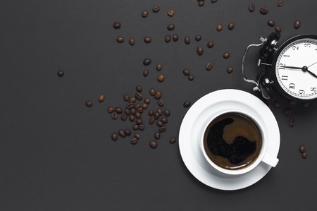 Flat lay cup of black coffee, coffee beans, black alarm clock on gray dark background top view copy space. Minimalistic food concept, morning breakfast, time to work, hot drink coffee backgroundの写真素材