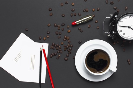 Flat lay cup black coffee, coffee beans, black alarm clock, red lipstick, color pencils, white cards on gray dark background top view copy space. Creative Concept time to work female desktopの写真素材