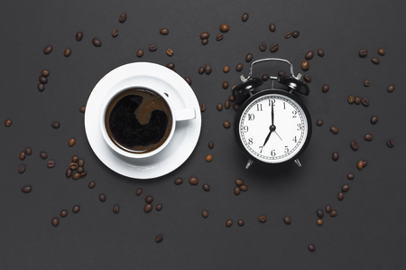 Flat lay cup of black coffee, coffee beans, black alarm clock on gray dark background top view copy space. Minimalistic food concept, morning breakfast, time to work, hot drink coffee backgroundの写真素材