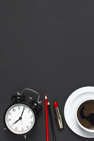 Flat lay cup black coffee, coffee beans, black alarm clock, red lipstick, color pencils on gray dark background top view copy space. Concept time to work female desktop Minimalistic coffee backgroundの写真素材