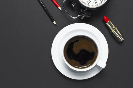 Flat lay cup black coffee, coffee beans, black alarm clock, red lipstick, color pencils on gray dark background top view copy space. Concept time to work female desktop Minimalistic coffee backgroundの写真素材