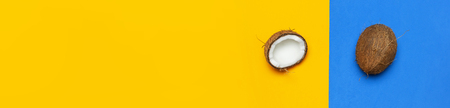 Ripe coconut on yellow and blue colored background, minimal flat lay style top view with copy space. Pop art design, creative summer and food concept Tropical fruit whole and half abstract backgroundの写真素材