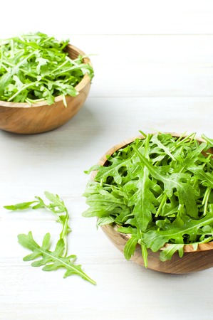 Fresh green arugula leaves on wooden bowl, rucola salad on white wooden rustic background with place for text. Selective focus. Rocket salad or arugula, healthy food, diet. Nutrition conceptの写真素材