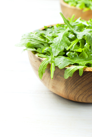 Fresh green arugula leaves on wooden bowl, rucola salad on white wooden rustic background with place for text. Selective focus. Rocket salad or arugula, healthy food, diet. Nutrition conceptの写真素材