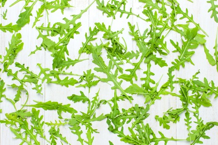 Fresh green arugula leaves, rucola salad on white wooden rustic background top view Flat lay with place for text. Rocket salad or arugula, healthy food, diet. Nutrition conceptの写真素材