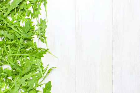 Fresh green arugula leaves, rucola salad on white wooden rustic background top view Flat lay with place for text. Rocket salad or arugula, healthy food, diet. Nutrition conceptの写真素材