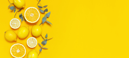 Ripe juicy lemons, orange and green eucalyptus twigs on bright yellow background. Lemon fruit, citrus minimal concept, vitamin C. Creative summer minimalistic background. Flat lay, top view copy spaceの写真素材