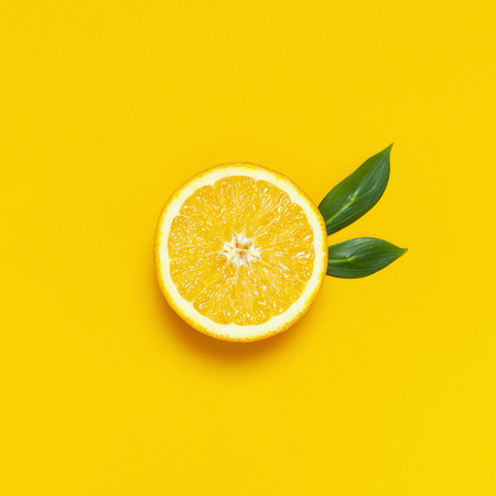 Ripe juicy orange and green leaves on bright yellow background. Orange fruit, citrus minimal concept, vitamin C. Creative summer food minimalistic background. Flat lay, top view, copy spaceの写真素材