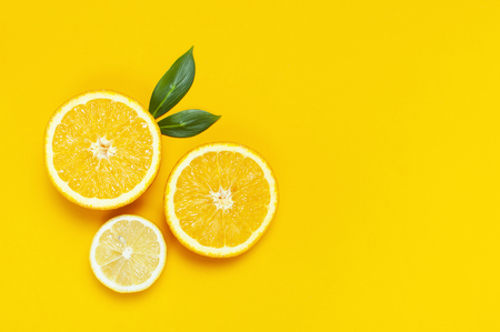 Ripe juicy lemons, orange and green leaves on bright yellow background. Lemon fruit, citrus minimal concept, vitamin C. Creative summer minimalistic background. Flat lay, top view, copy spaceの写真素材