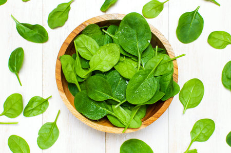 Fresh green spinach leaves on wooden bowl on white wooden rustic background top view copy space....