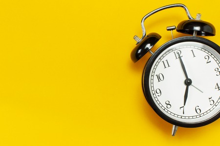 Black retro alarm clock on yellow background top view Flat lay copy space. Minimalistic background, concept of time, deadline, time to work, morning.の写真素材