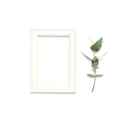 White wooden photo frame and green eucalyptus leaves on white background. Flat lay top view copy space. Stylish minimal composition, artwork mockup, picture frame, home decoration.の写真素材