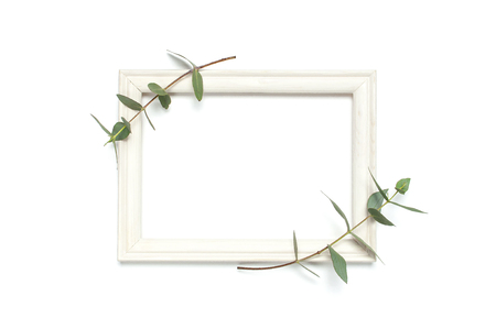White wooden photo frame and green eucalyptus leaves on white background. Flat lay top view copy space. Stylish minimal composition, artwork mockup, picture frame, home decoration.の写真素材