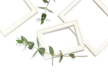 White wooden photo frame and green eucalyptus leaves on white background. Flat lay top view copy space. Stylish minimal composition, artwork mockup, picture frame, home decoration.の写真素材