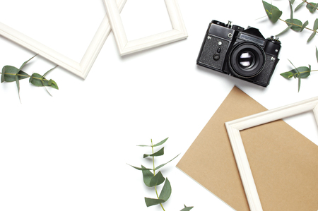 White photo frame old retro camera notebook diary green eucalyptus leaves on white background. Flat lay top view copy space. Stylish minimal composition artwork mockup picture frame home decoration.の写真素材