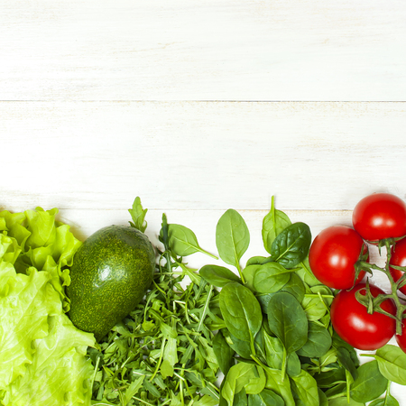 Fresh green spinach leaves, arugula rucola, avocado, cherry tomatoes and lettuce leaves on white wooden rustic background top view copy space. Ingredient for salad healthy food diet Nutrition conceptの写真素材