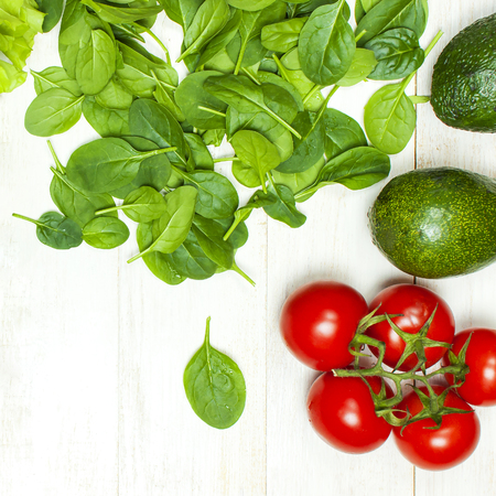 Fresh green spinach leaves, arugula rucola, avocado, cherry tomatoes and lettuce leaves on white wooden rustic background top view copy space. Ingredient for salad healthy food diet Nutrition conceptの写真素材