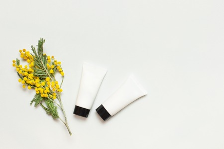 White cosmetic bottle containers with yellow Mimosa flowers on light background top view flat lay. Cosmetics SPA branding mock-up, Natural organic beauty product concept, Minimalism cosmetics style.の写真素材